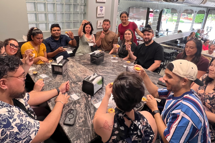 Group of people sitting around a table in a cafe, holding pastries and smiling.