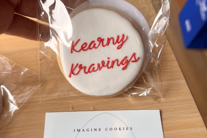 Cookie labeled 'Kearny Kravings' and business card on wooden table.